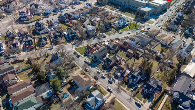Aerial view capturing a suburban area with numerous houses, parallel streets, parked cars, and scattered trees, illustrating the detailed layout of a well established residential zone