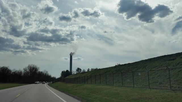 Driving Toward Smokestack Under Cloudy Sky on Quiet Road