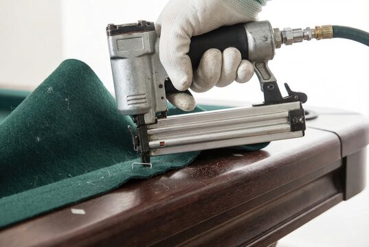 Hand wearing white glove using pneumatic staple gun to attach green felt to pool table
