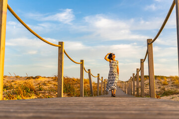 Fototapeta premium Woman walking on boardwalk to beach dunes at sunset
