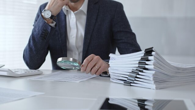 Professional accountant or auditor carefully examining financial documents and corporate reports with a magnifying glass, diligently researching tax obligations and legal compliance. Audit and taxes