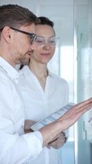 Fototapeta premium Business colleagues collaborating in a meeting, pointing at a glass board and reviewing charts on a tablet as they strategize, analyze data and plan next steps together