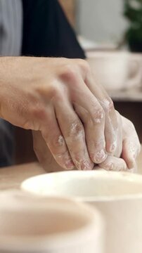 Close view hands shaping clay while forming small bowl. Person molding soft material with fingers. Craft process creating pottery piece in workshop. Detailed texture visible on wet clay surface.