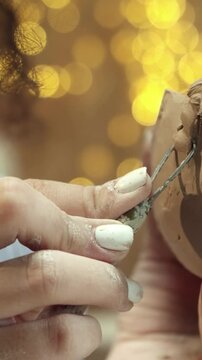 Close view of hands carving clay bowl edge with tool. Person removing excess material and shaping surface. Refining ceramic form and smoothing details. Working in pottery workshop.