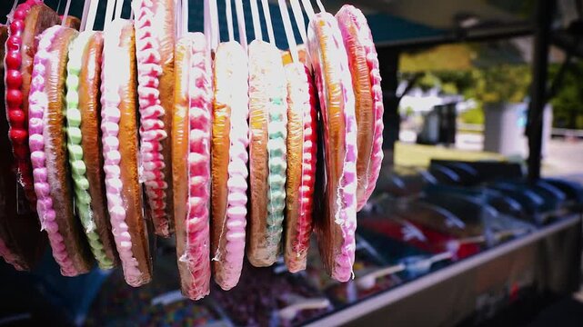 Seitliche Nahaufnahme von sich drehenden Lebkuchenherzen mit bunter Zuckerglasur vor unscharfem S&uuml;&szlig;igkeitenstand auf einem sonnigen Jahrmarkt oder Oktoberfest