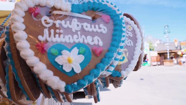 Lebkuchenherzen mit Schriftzug &bdquo;Gru&szlig; aus M&uuml;nchen&ldquo; in blau wei&szlig;er Zuckerglasur an einem Verkaufsstand auf dem Oktoberfest, sonniger Tag mit traditioneller Dekoration