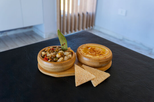Aperitivos mediterr&aacute;neos servidos en un ambiente interior moderno. Un tentempi&eacute; vegano saludable con hummus y lentejas en cuencos de madera.El fondo difuminado de una casa crea una atm&oacute;sfera acogedora