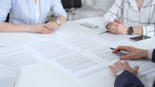 Business partners discussing contract terms, reviewing legal documents during an office meeting, focusing on agreement details and professional negotiation strategies