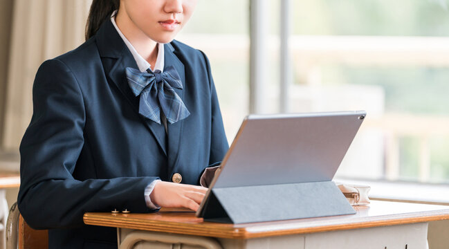 Female middle and high school students in their school uniforms studying using tablets.