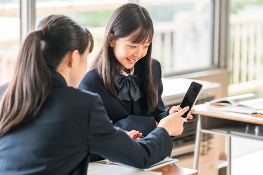 A middle school girl talking while looking at her smartphone in a school classroom.