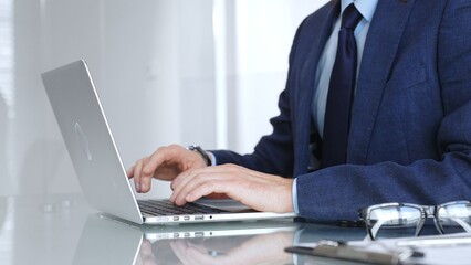 Fototapeta premium Professional businessman working on laptop computer, typing on keyboard in modern office, managing business tasks. Business people concept