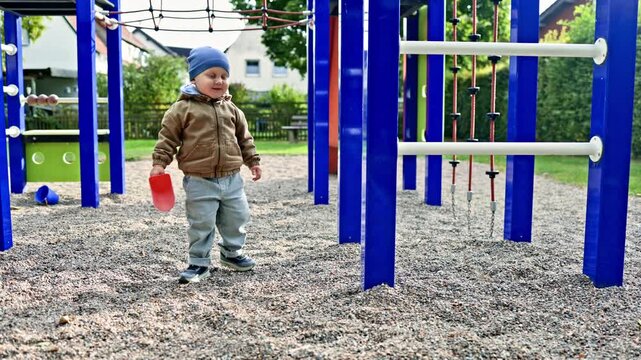 Cute 2 year old boy playing outside on the playground. Toddler playing outdoors and exploring the environment. Child having fun and being independent.