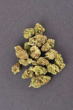 Dried cannabis buds arranged on a plain gray surface, showcasing their green and orange hues and dense texture.