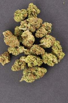 Close-up of dried cannabis buds with green and orange hues arranged on a dark surface.