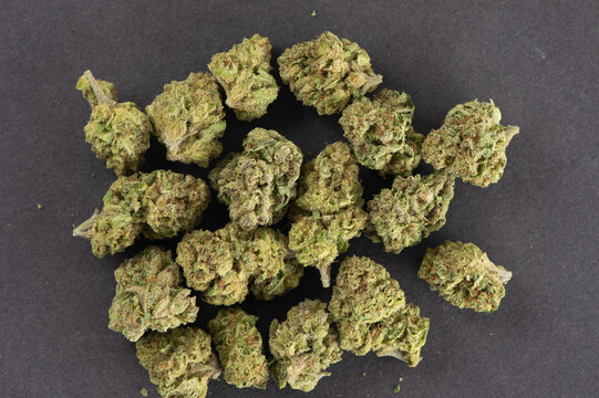 Several dried cannabis buds arranged on a dark surface.