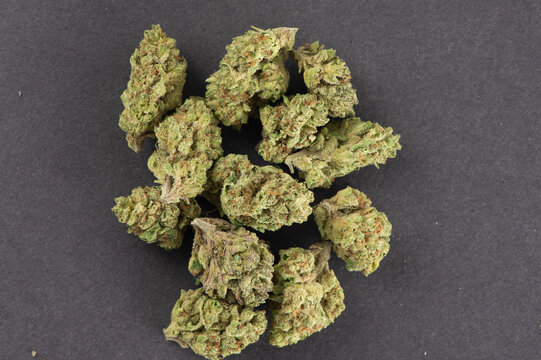 Dried cannabis buds with green and orange hues displayed on a dark surface.