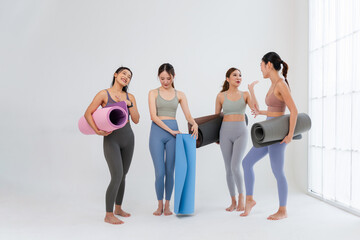 Obraz premium Group of young asian women in sportswear holding yoga mats and talking in bright studio, Happy diverse group of female friends preparing for yoga class or pilates workout, Healthy lifestyle