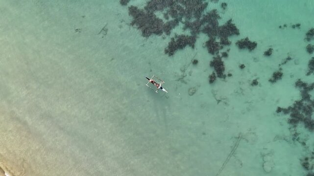 Overhead helix drone shot circling two fishermen casting a net from a small boat in clear shallow waters at Liminangcong, Philippines