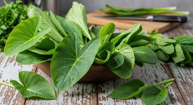 Freshly Harvested Green Taro Leaves and Other Vegetables on a Rustic Wooden Table.