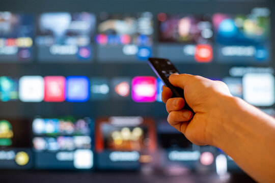 Hand Holding TV Remote Toward Blurred Smart TV Streaming Screen