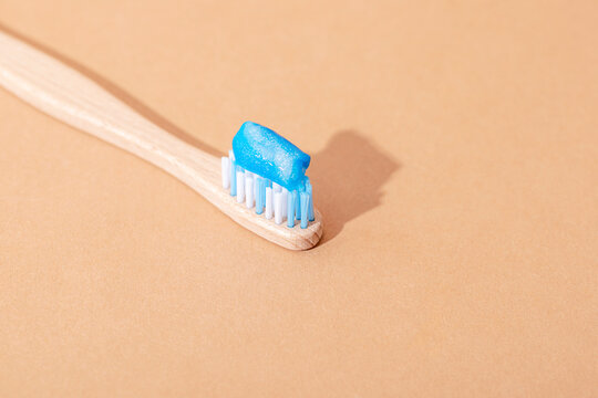 Bamboo toothbrush with blue toothpaste on beige background, eco friendly oral care concept. Top view, copy space