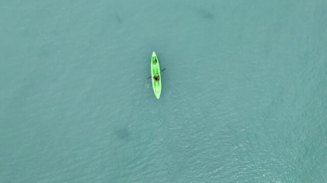 Overhead tracking drone shot of a person paddling a green kayak near the shore of Dipnay in clear shallow waters, Philippines