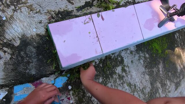 First-person clip pulling weeds bare-handed around the pink floor. Video of cleaning a weed growing in a crack in the cement of the steps in steady 4K resolution.