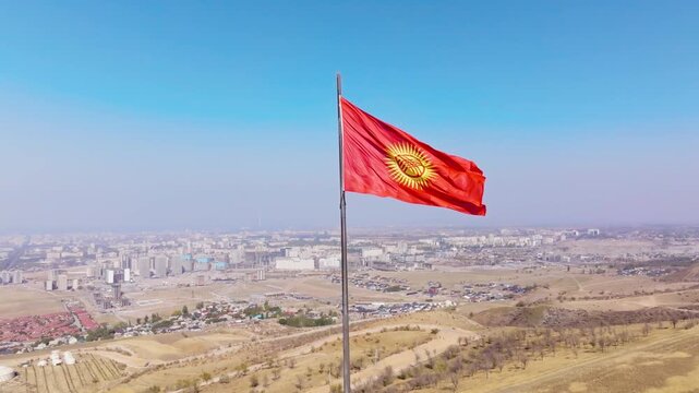 National Kyrgyzstan Flag Over Dry Hills near Bishkek City, aerial view with pulling back camera movement.