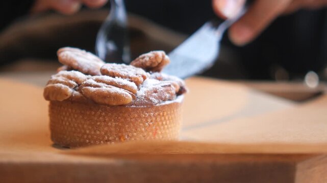 Close up video of person hands eating delicious pecan nuts tart with knife and fork on wooden board.