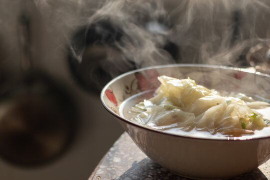 A bowl of hot cabbage soup with thick steam rising up under natural sunlight creating a cozy domestic meal atmosphere
