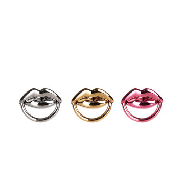 Three metallic lip-shaped objects in silver, gold, and pink against a black background