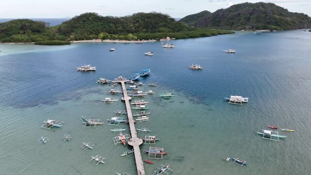 Flyover drone shot of Linapacan proper showing a coastal community beside turquoise waters with Patoyo Island ahead, Philippines