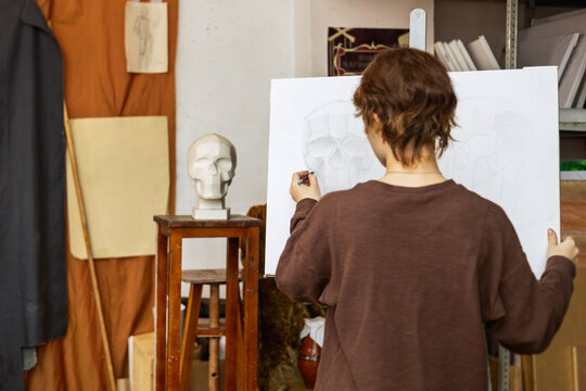 A female artist paints a human skull from a plaster cast. Real photo of an art studio.