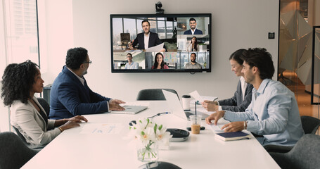 Diverse international business team discussing teamwork, work strategy, planning deal, partnership on online hybrid video conference, meeting at table and large screen, talking © fizkes