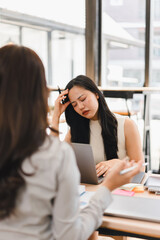Obraz premium Stressed Asian businesswoman suffering from headache while working on laptop during office meeting with colleague