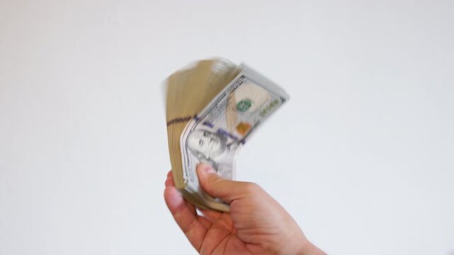 Adult man displays thick stack of paper currency against plain white background. Neutral expression evokes feelings of wealth and success.