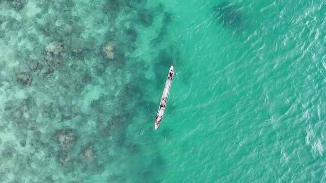 Overhead tracking drone shot of two fishermen paddling a canoe over the crystal clear turquoise waters of Linapacan, Palawan, Philippines