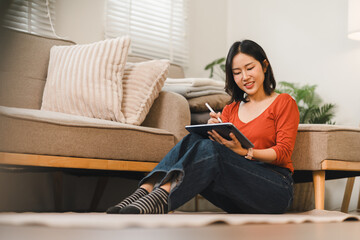 Young Asian woman using digital tablet and stylus while sitting on the floor in a living room © PRIME STOCK LAB