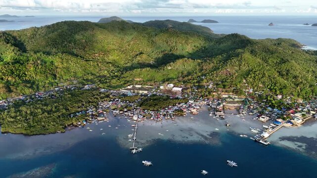 Morning panning drone shot of San Miguel town in Linapacan, showing a peaceful coastal community surrounded by calm blue waters and natural terrain, Philippines