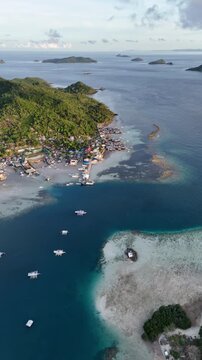 Portrait panning aerial shot of Linapacan coastal channel featuring the local port, seaside community, and contrast between deep blue and turquoise shallow waters, Philippines