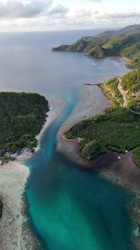 Portrait panning drone shot over Linapacan coastal channel highlighting the vivid contrast between deep blue ocean and shallow turquoise waters in the morning light, Philippines