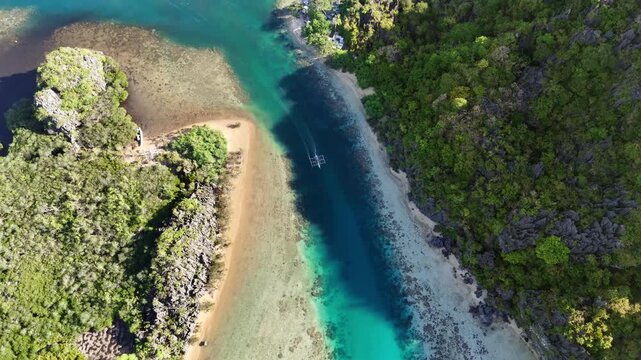 360-degree top-down drone shot of an outrigger boat crossing a narrow channel with striking shallow and deep water contrast in Linapacan, Palawan, Philippines