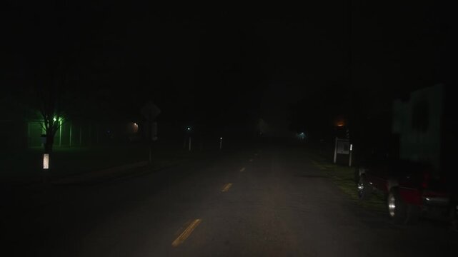Driving along empty foggy night street with houses and signs, forward motion along the road through thick fog creates atmosphere of night travel low visibility and quiet residential area