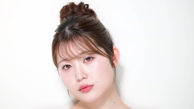 透明感のあるツヤ肌と潤いのある美しい肌の若い女性のホワイトニングの美白美容とスキンケアイメージクローズアップカメラ目線　アップヘアのお団子かわいい動画　スローモーション
