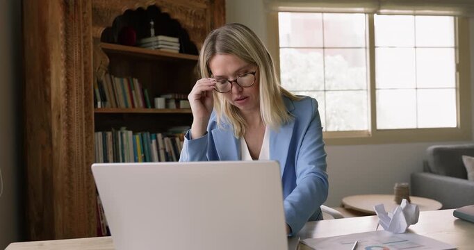 Overworked tired young businesswoman in glasses typing on laptop, taking off glasses, sighing, feeling stressed, exhausted, headache attack, touching head, temples with closed eyes
