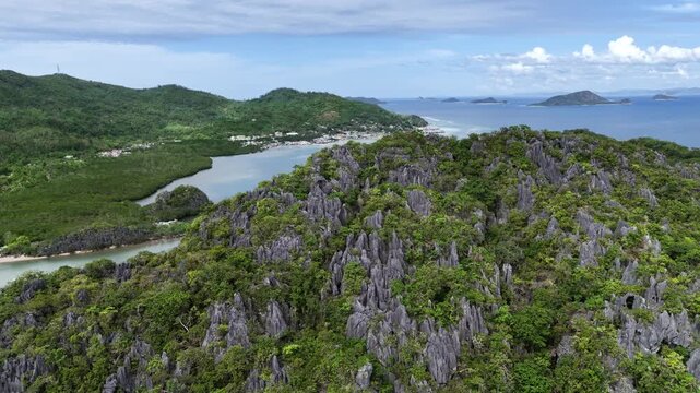 Pull-away aerial shot over Ile Island revealing limestone formations covered in lush vegetation with Linapacan town visible in the background, Philippines