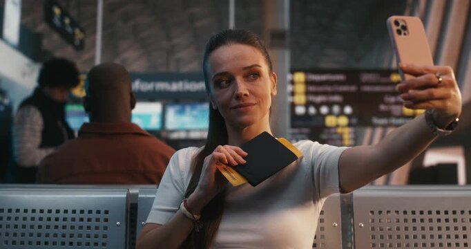 Woman Holds Paper Boarding Pass and Smartphone to Take Selfie in Airport Terminal. Female Captures Memory of Upcoming Journey to Share on Social Media. Digital Lifestyle, and Personal Storytelling.