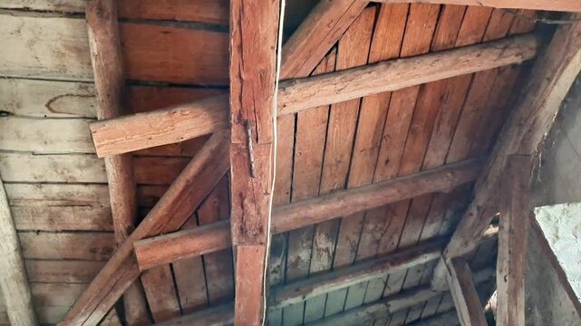 Aged wooden beams and planks arranged in triangular truss pattern, dim lighting highlighting rustic textures, capturing the worn detail of an old attic or barn roof
