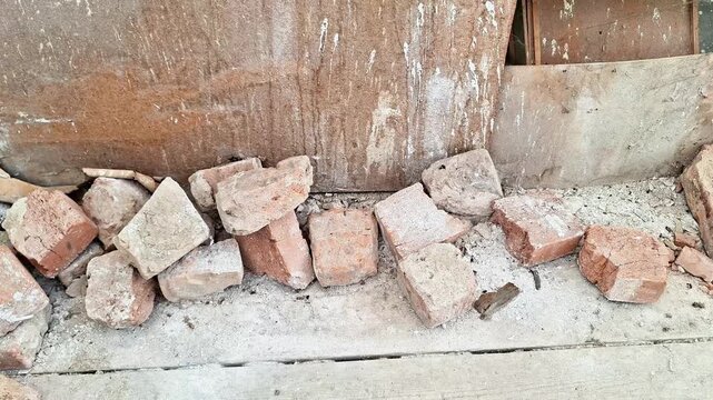 Row of broken bricks scattered on dusty concrete floor against stained plaster wall, rough textures and cracks highlighting decay and neglected atmosphere of old structure