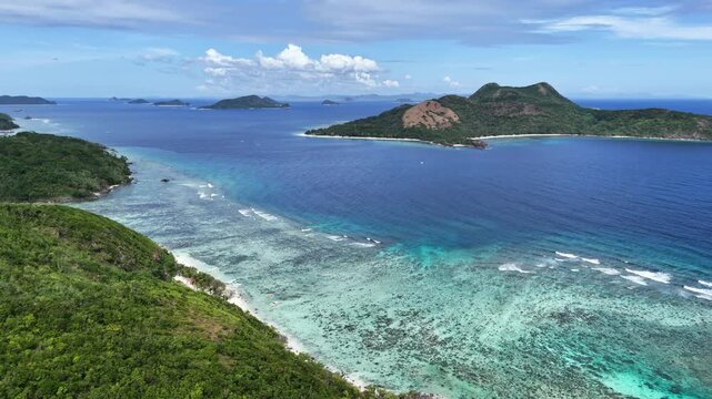 Push-in aerial shot above Ile Island heading toward Patoyo Island, revealing crystal clear waters and a sunlit coastline washed by gentle waves, Philippines